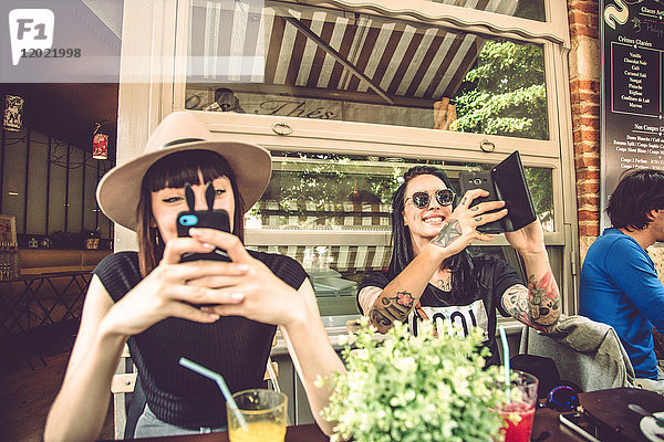 Porträt von zwei jungen Frauen  die auf einer Restaurantterrasse sitzen und Selfies machen