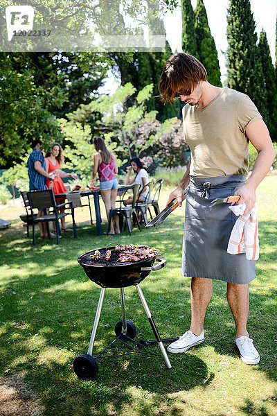 Gut aussehender junger Mann  der bei einer Grillparty im Garten während des Sommerurlaubs Fleisch zubereitet.