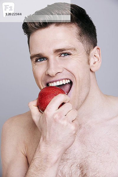 Oben-ohne-Mann  in einen Apfel beißend  in die Kamera schauend  lächelnd