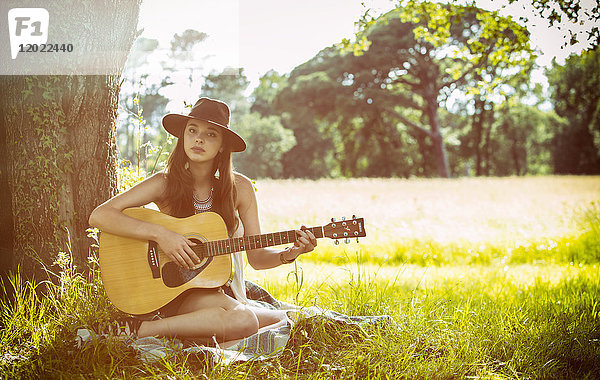 Junge Frau sitzt im Gras und spielt Gitarre