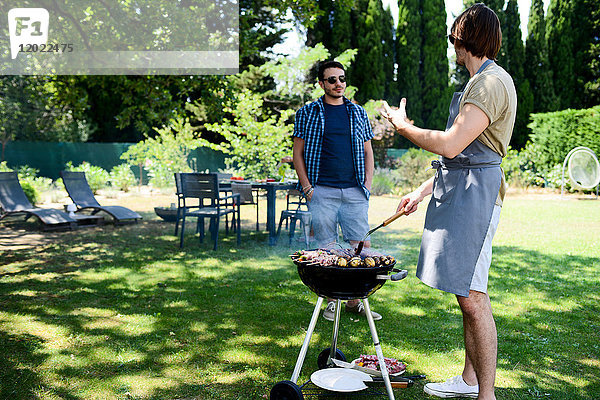 Gut aussehender junger Mann  der bei einer Grillparty im Garten während des Sommerurlaubs Fleisch zubereitet.