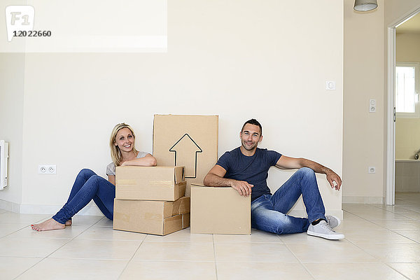 Ein glückliches junges Paar trägt Kartons und zieht in sein neues Haus ein.