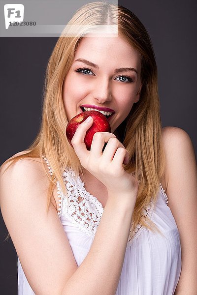 Porträt einer lächelnden jungen Frau  die in einen Apfel beißt