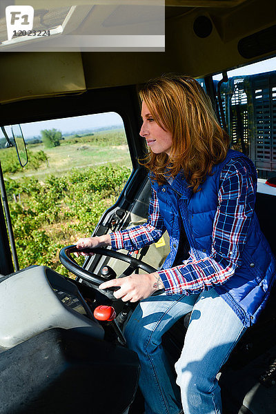 schöne und fröhliche junge Bäuerin beim Traktorfahren auf den Feldern während der Ernte auf dem Lande