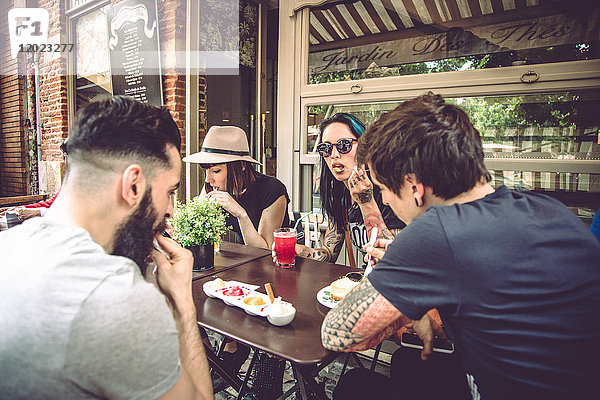 Gruppe junger Hipster  die auf einer Restaurantterrasse sitzen  essen und trinken