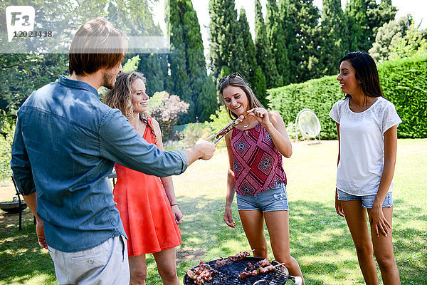 Eine Gruppe glücklicher und fröhlicher junger Leute  die sich während einer Sommerferienparty im Garten am Grill vergnügen.
