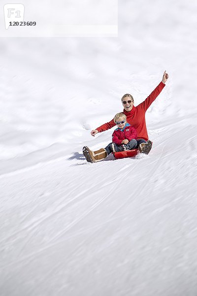 Porträt einer lächelnden Frau  die mit ihren Kindern auf einem Schlitten im Schnee sitzt  Crans-Montana  Schweizer Alpen  Schweiz