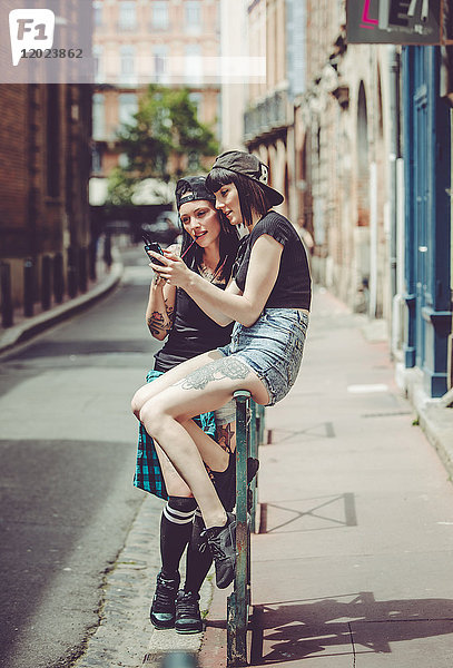 zwei junge Frauen  die in einer Stadtlandschaft von einem Mobiltelefon gefesselt sind