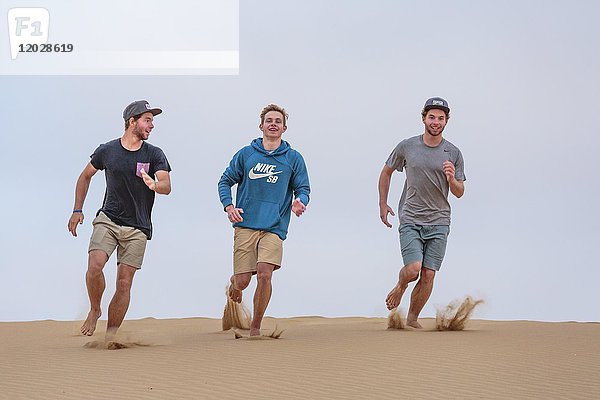 Drei junge Männer laufen eine Sanddüne hinunter  Namib-Wüste  Namibia  Afrika