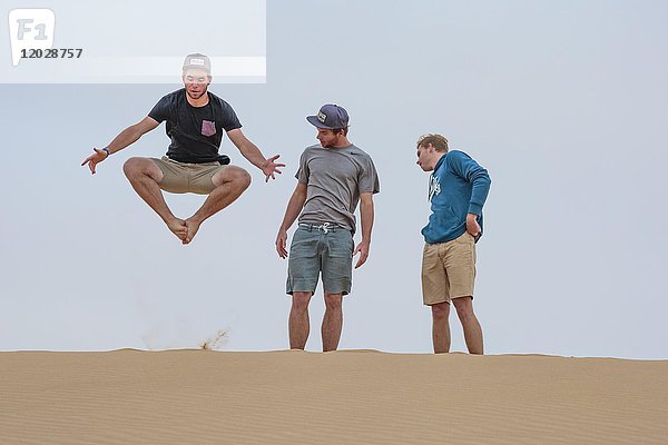 Junger Mann springt auf Sanddüne  zwei schauen zu  Namibia  Afrika