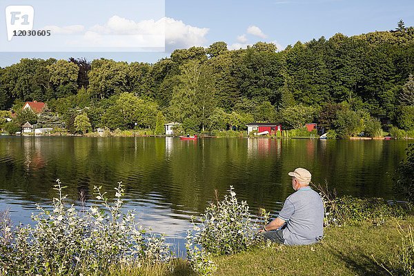 Mann  Senior sitzt am Seeufer  Tiefenwarensee  Waren  Müritz  Mecklenburgische Seenplatte  Mecklenburg Vorpommern  Deutschland  Europa