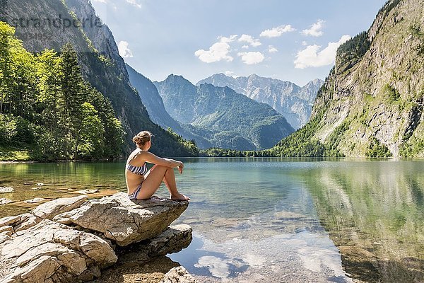 Junge Frau sitzt in Badekleidung am Obersee  Watzmann und Bergkulisse  Berchtesgadener Alpen  Nationalpark Berchtesgaden  Oberbayern  Bayern  Deutschland  Europa