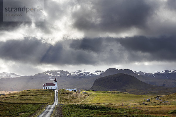 Ingjaldsholskirkja vor der Kulisse der Berge an einem dramatischen  stürmischen Tag  in der Nähe von Rif  Snaefellsnes-Halbinsel  Island  Polarregionen