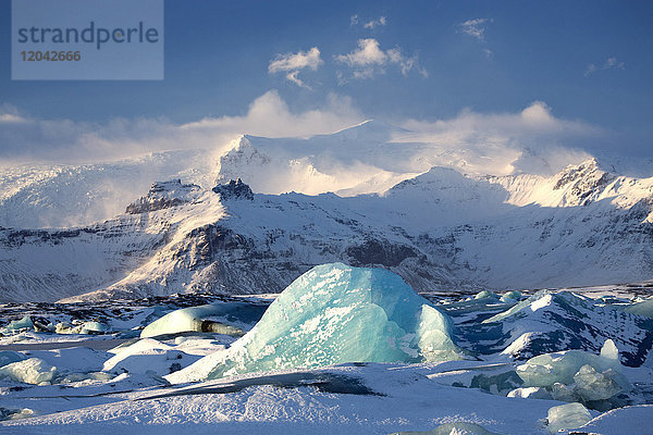Winterlicher Blick über die zugefrorene Gletscherlagune Jokulsarlon mit blauen  schneebedeckten Eisbergen und fernen Bergen  Südisland  Polarregionen