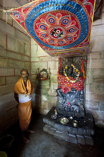 Hindu-Priester in safranfarbenen Gewändern am Radha-Krishna-Schrein in einem winzigen ländlichen Tempel  Chaurasi  Prachi Valley  Odisha  Indien  Asien