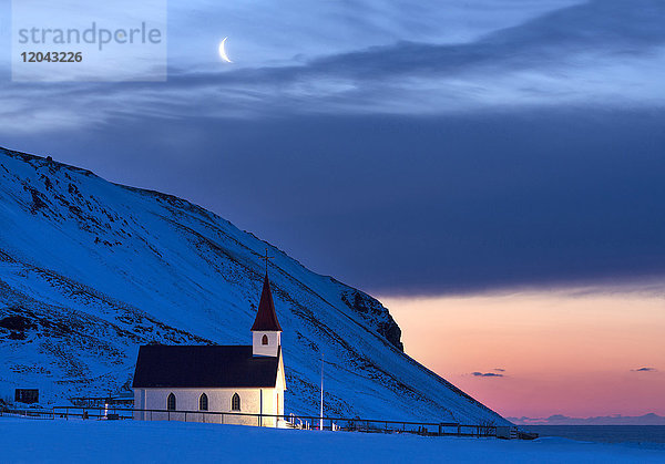 Beleuchtete Kirche in der Morgendämmerung vor schneebedeckten Bergen  Winter  bei Vik  Südisland  Polarregionen