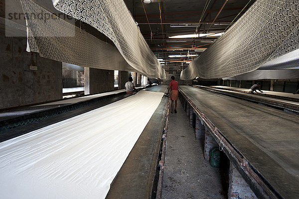 Baumwollgewebe wird auf dem Drucktisch für den Siebdruck vorbereitet  bedruckte Bolzen hängen zum Trocknen darüber  Bagru  Rajasthan  Indien  Asien