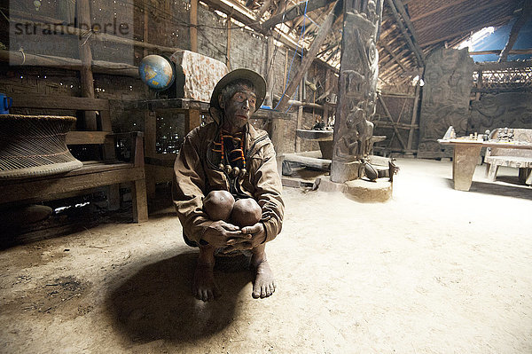 Naga-Mann  Longsha Wangnao  Kopfjäger  mit tätowiertem Gesicht und Naga-Halskette  sitzend im Gemeinschaftshaus eines Naga-Stammes  Longwa  Nagaland  Indien  Asien