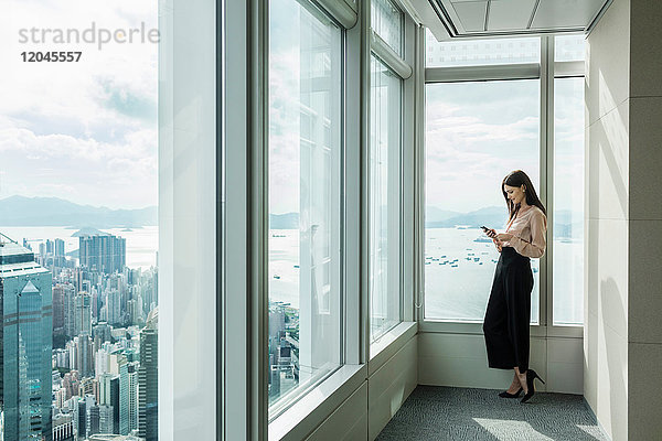 Geschäftsfrau im Bürofenster eines Wolkenkratzers mit Smartphone