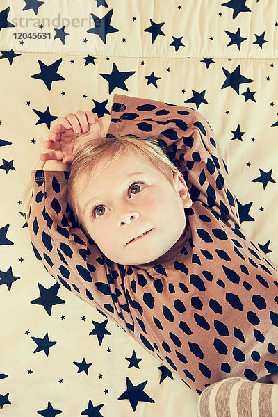 Porträt eines weiblichen Kleinkindes  das auf einem Bett mit Sternenmuster liegt und nach oben schaut