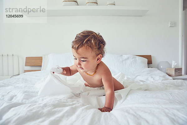 Kleinkind sitzt auf dem Bett und hält aufgetrennte Toilettenpapierrolle