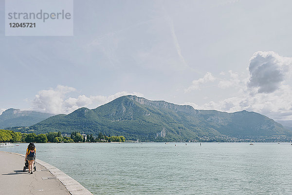 Rückansicht einer Frau beim Spaziergang mit Kinderwagen am Ufer des Sees von Annecy  Annecy  Auvergne-Rhone-Alpes  Frankreich