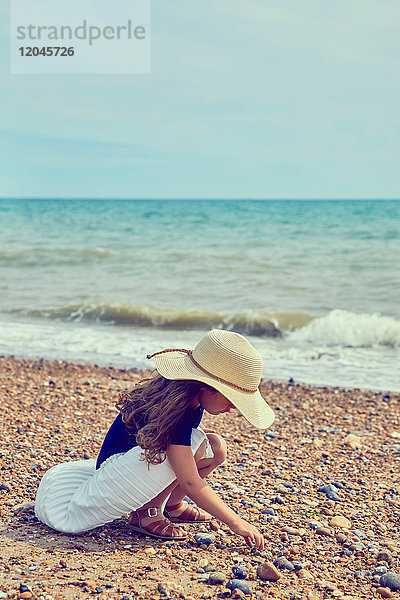 Junges Mädchen kauert am Strand und sammelt Muscheln