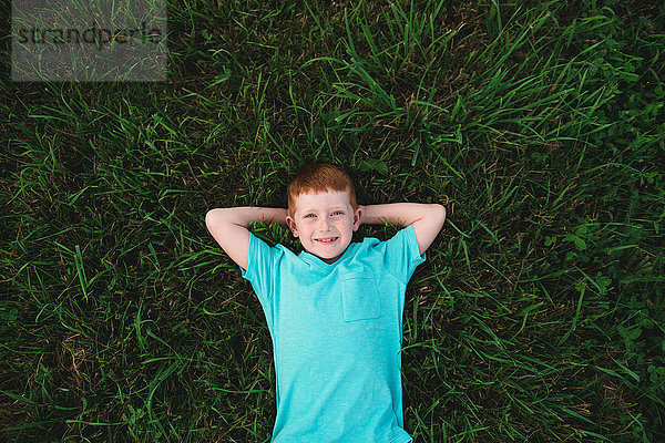 Portrait eines auf Gras liegenden rothaarigen Jungen