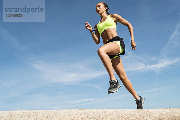 Niedrigwinkelansicht einer jungen Läuferin  die entlang der Seemauer gegen blauen Himmel läuft