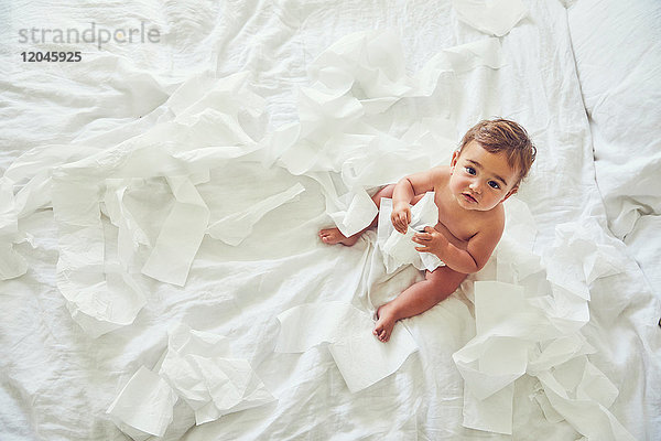 Kleinkind sitzt auf dem Bett und hält aufgetrennte Toilettenpapierrolle