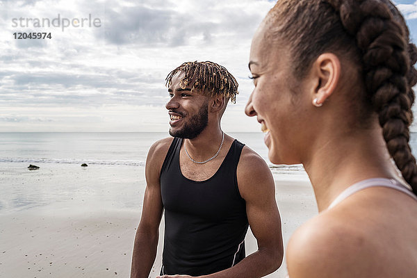 Junge männliche und weibliche Läufer lächeln am Strand