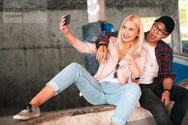 Junges Skateboard-Paar sitzt auf der Rampe und nimmt Smartphone-Selfie