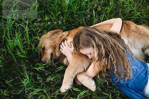 Draufsicht auf ein auf Gras liegendes Mädchen  das den Golden Retriever Dog umarmt.