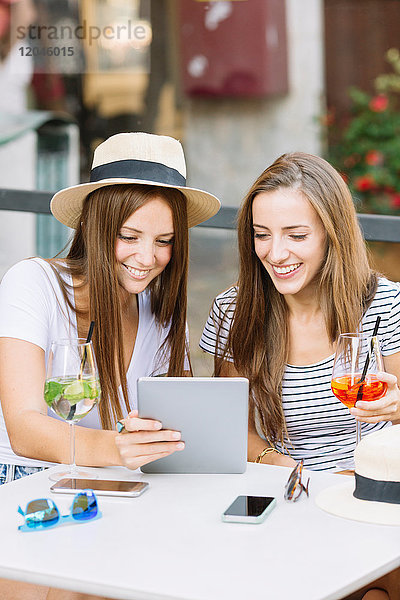 Zwei junge Freundinnen schauen sich im Straßencafé ein digitales Tablet an