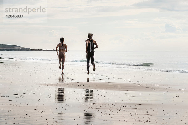 Rückansicht junger männlicher und weiblicher Läufer  die barfuss am Strand entlang laufen