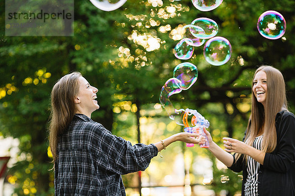 Zwei junge Freundinnen machen im Park schwebende Blasen
