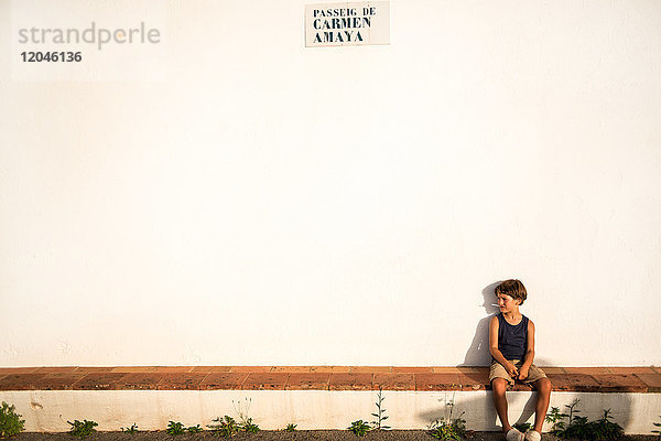 Junge sitzt auf Mauer vor weißer Kirche