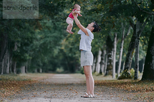 Frau hält eine kleine Tochter im baumbestandenen Park hoch  Chenonceaux  Loiretal  Frankreich
