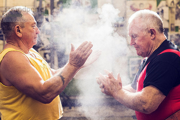 Zwei ältere männliche Kraftdreikämpfer kreiden ihre Hände in der Turnhalle