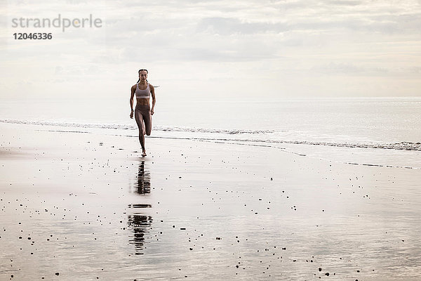 Junge Frau rennt am Strand entlang