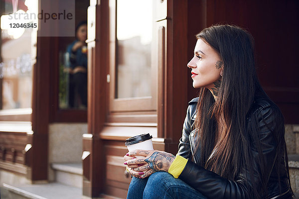 Junge Frau sitzt im Freien  hält Kaffeetasse  Tätowierungen auf Händen