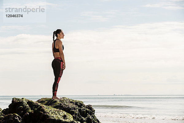 Junge Läuferin blickt vom Strandfelsen aufs Meer