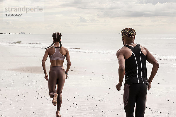 Rückansicht junger männlicher und weiblicher Läufer  die am Strand laufen