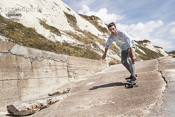 Junge männliche Skateboarder skateboarden an Klippe Seewand