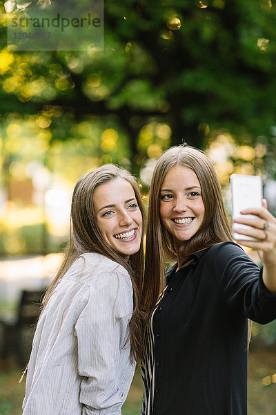 Zwei junge Freundinnen posieren für Smartphone-Selfie im Park