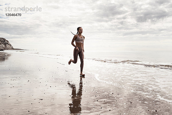 Junge Läuferin läuft am Strand barfuss am Wasser entlang