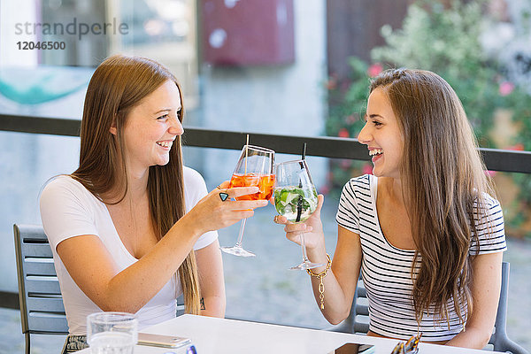 Zwei junge Freundinnen stoßen im Straßencafé auf einen Cocktail an
