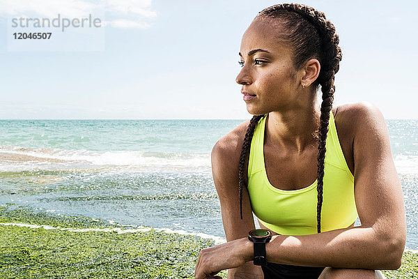 Junge Frau in Sportkleidung  am Meer kauernd