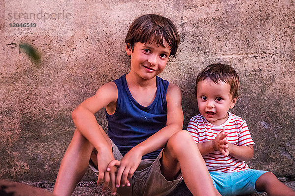 Porträt eines Jungen und eines kleinen Bruders  die an der Wand sitzen