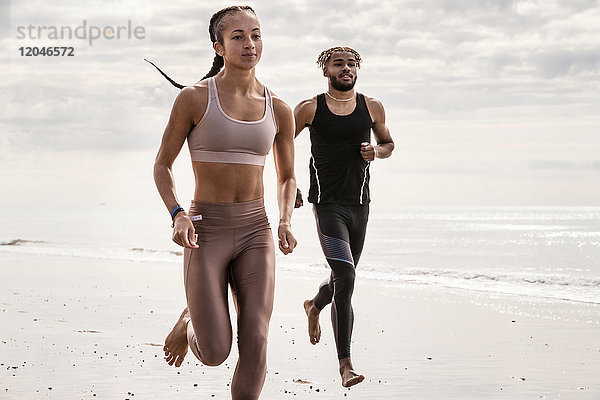 Junge männliche und weibliche Läufer laufen barfuss am Strand entlang